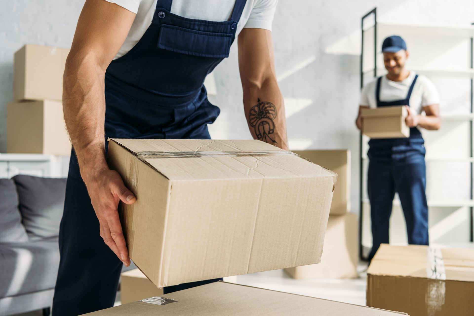 Moving workers carrying cardboard boxes inside a bright apartment.