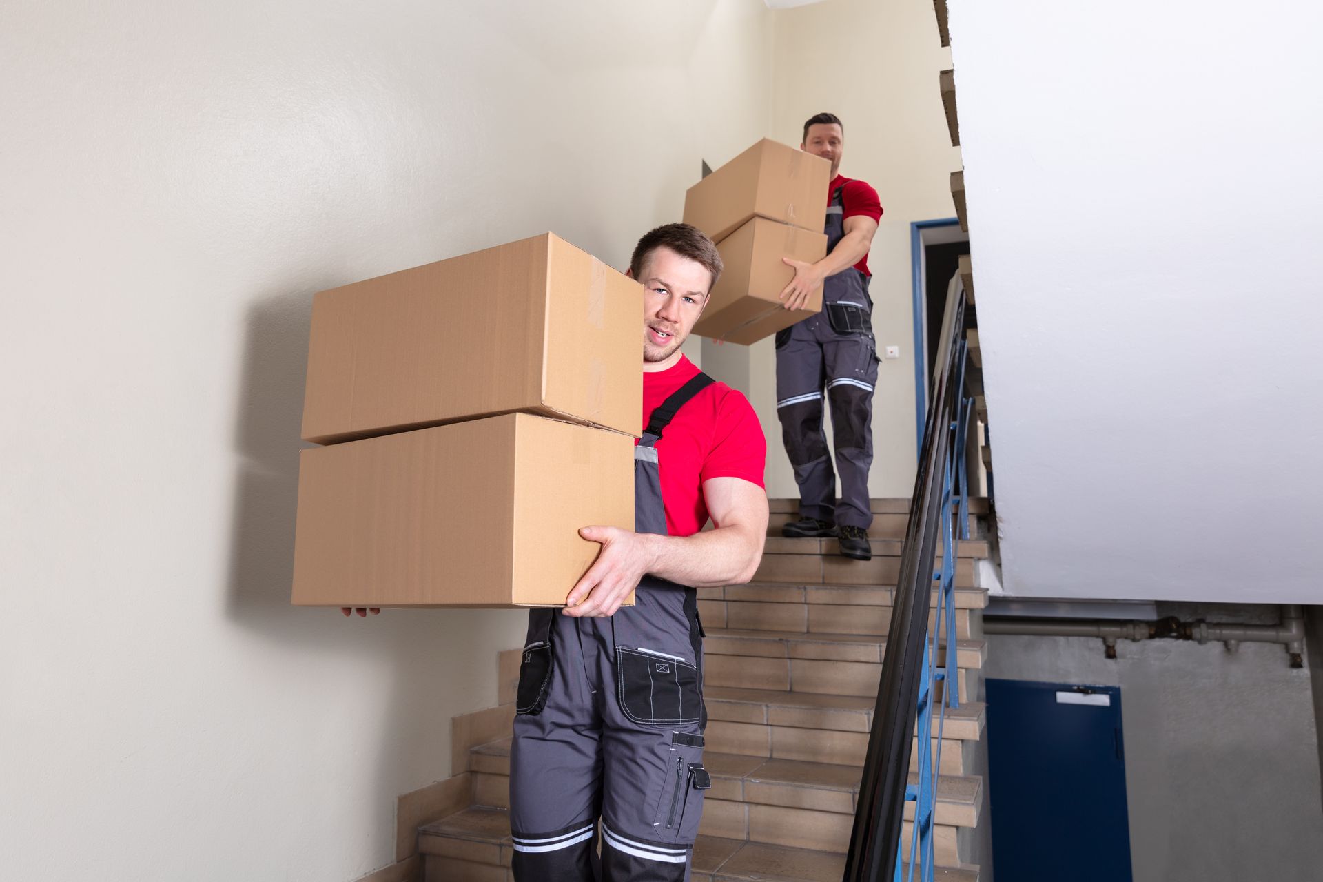 Professional movers carrying cardboard boxes down a stairwell during a residential move service team.