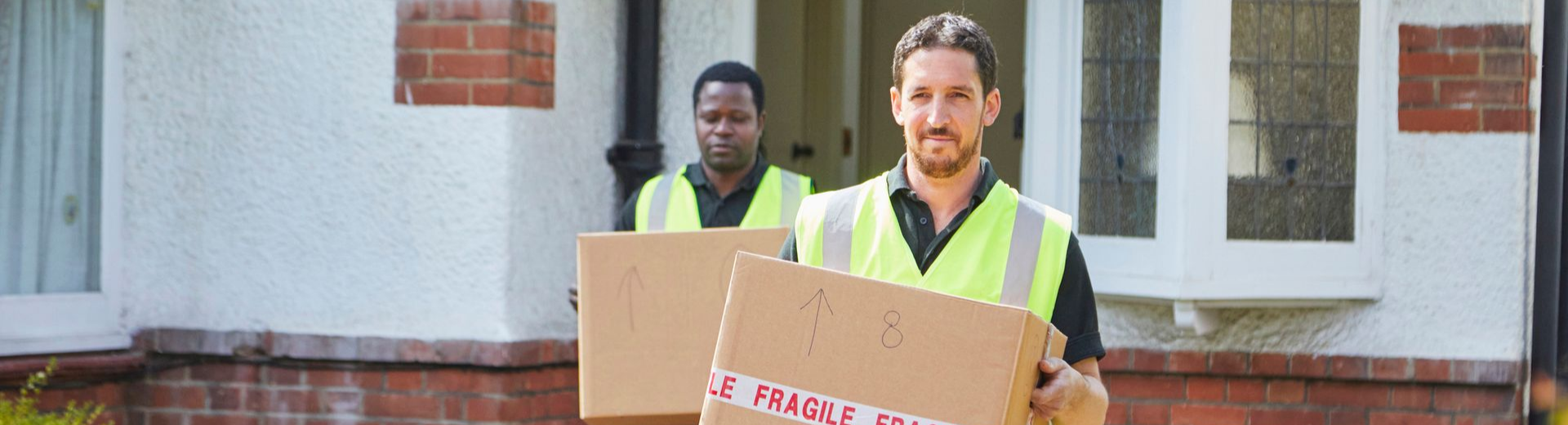 Two male movers providing residential services, wearing reflective vests and carrying boxes.