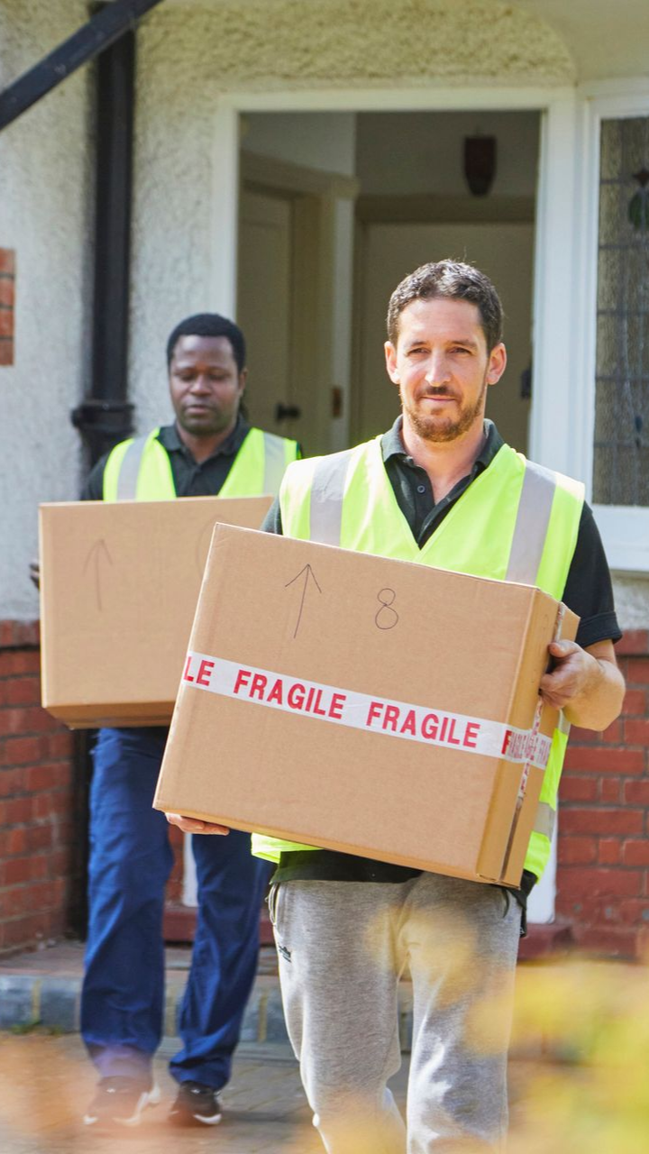 Two male movers providing residential services, wearing reflective vests and carrying boxes.