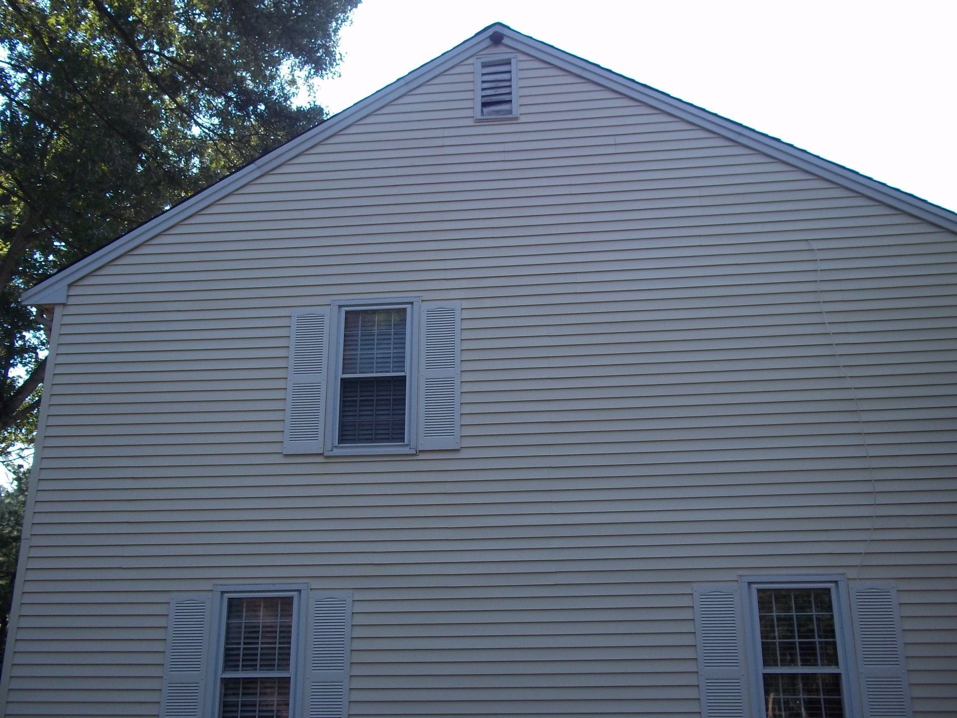 Side view of a white, multi-story vinyl-sided house exterior with several windows and a vertical pipe.
