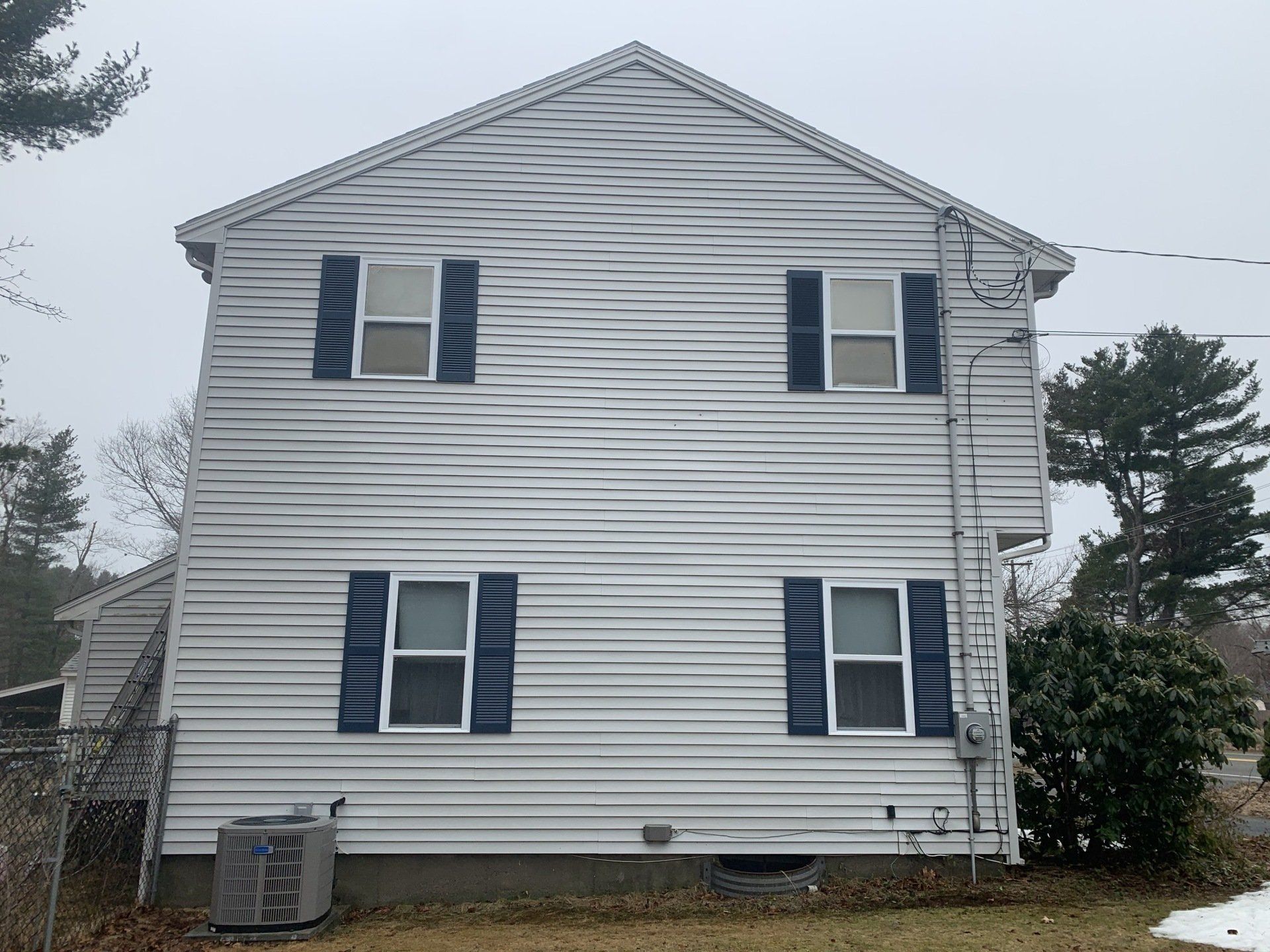 A two-story house exterior with gray horizontal siding, four windows with dark blue shutters, and a lawn in front.