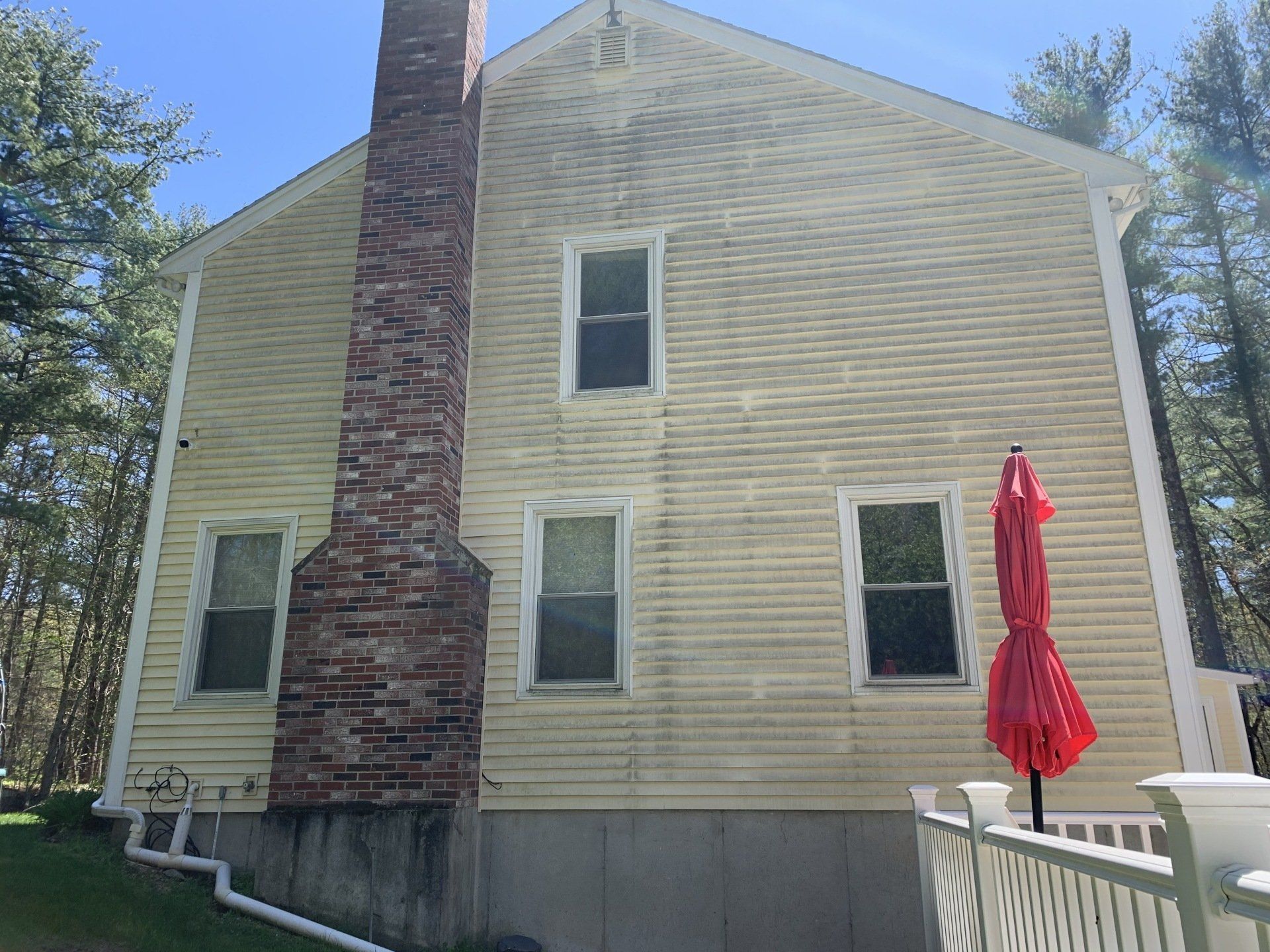 Yellow, two-story house with a brick chimney, three visible windows, and a red patio umbrella outdoors.