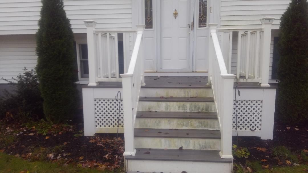 A front entrance with white railings and lattice skirting, featuring grey steps leading to a white door on a house.