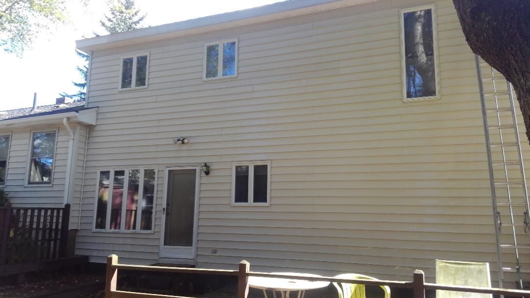 A two-story house exterior with gray horizontal siding, four windows with dark blue shutters, and a lawn in front.
