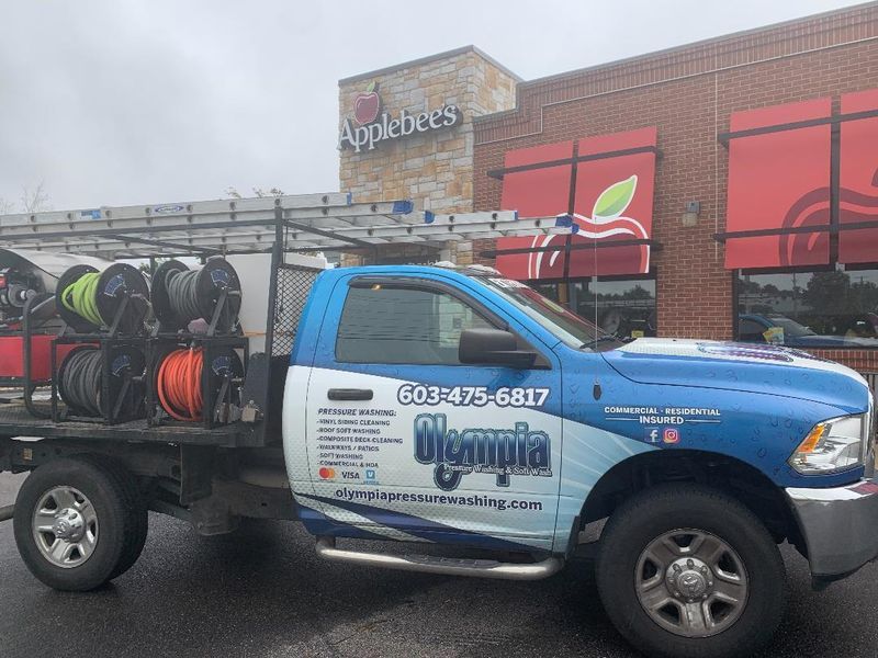 A blue and white service truck labeled Olympia Plumbing is parked in front of an Applebee's restaurant.