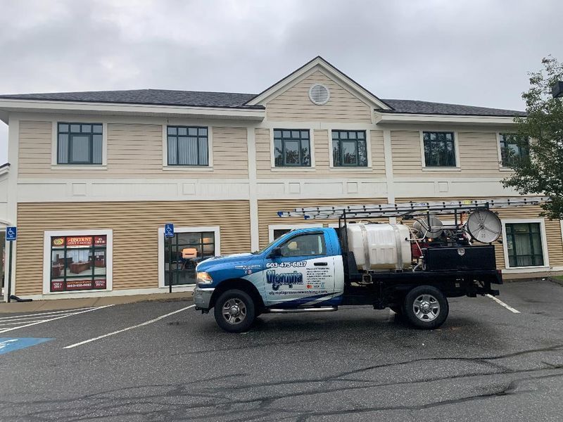A blue and white utility truck with a water tank parked in front of a two-story beige commercial building.