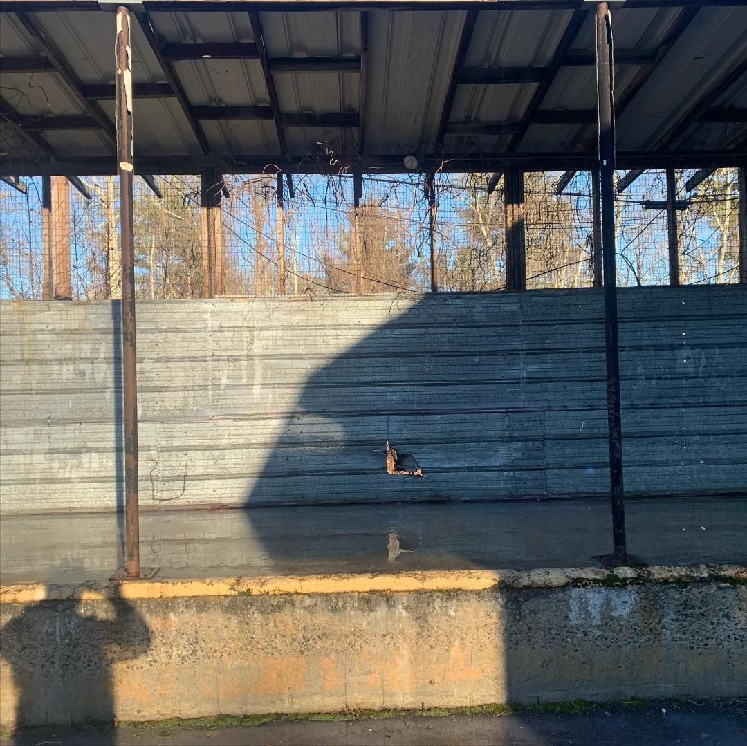 A sunlit covered loading dock with a textured concrete wall, metal framing, and a long shadow cast across the foreground.