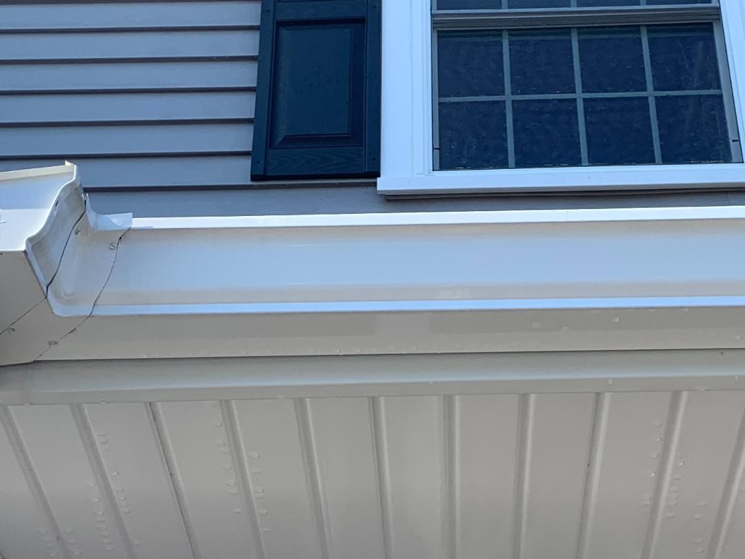 White exterior rain gutter showing dark streaks of oxidation and dirt buildup beneath a window with dark shutters.