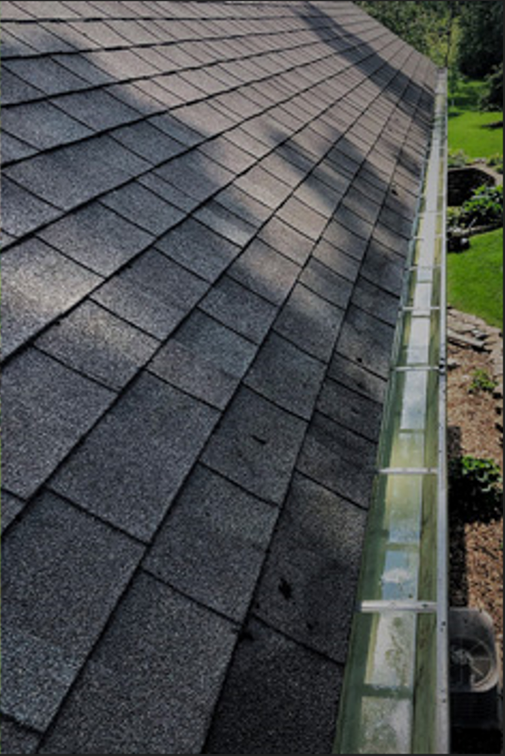 A high-angle view of a gray asphalt shingle roof leading to a clean, empty gutter running along the edge.