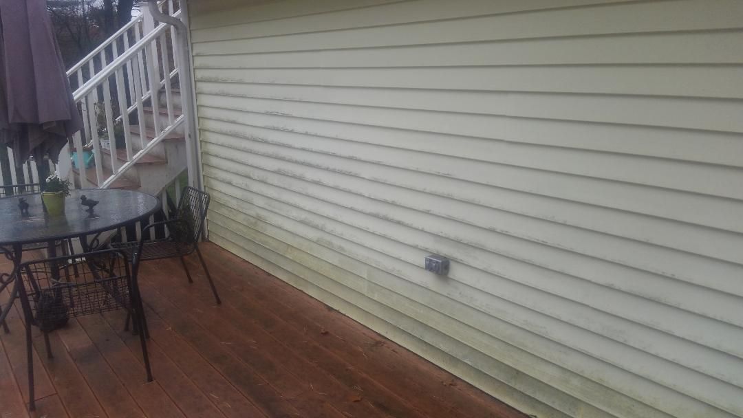 A light-yellow siding wall on a deck with a patio table and chairs, showing signs of dirt near the bottom.
