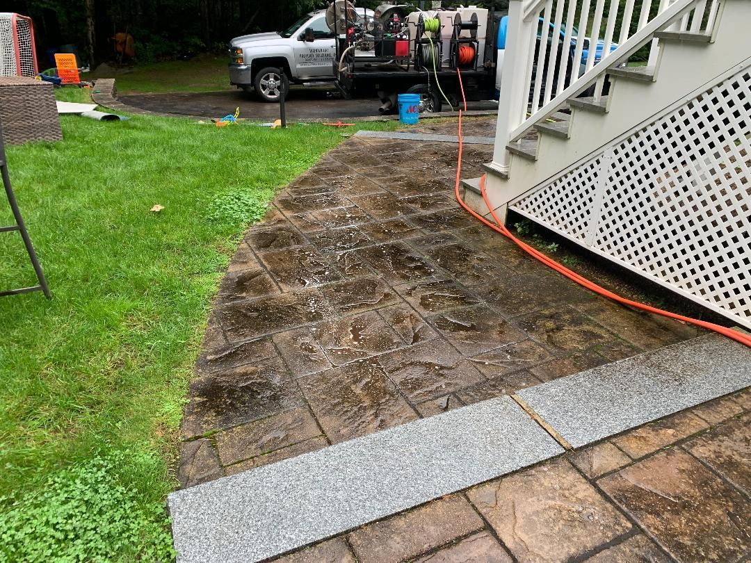 A pressure-washed outdoor stone patio path next to a white wooden staircase and a work truck in a grassy yard.