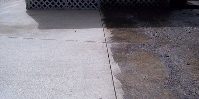 A split view of a driveway surface, showing clean concrete on the left and dark, stained concrete on the right.