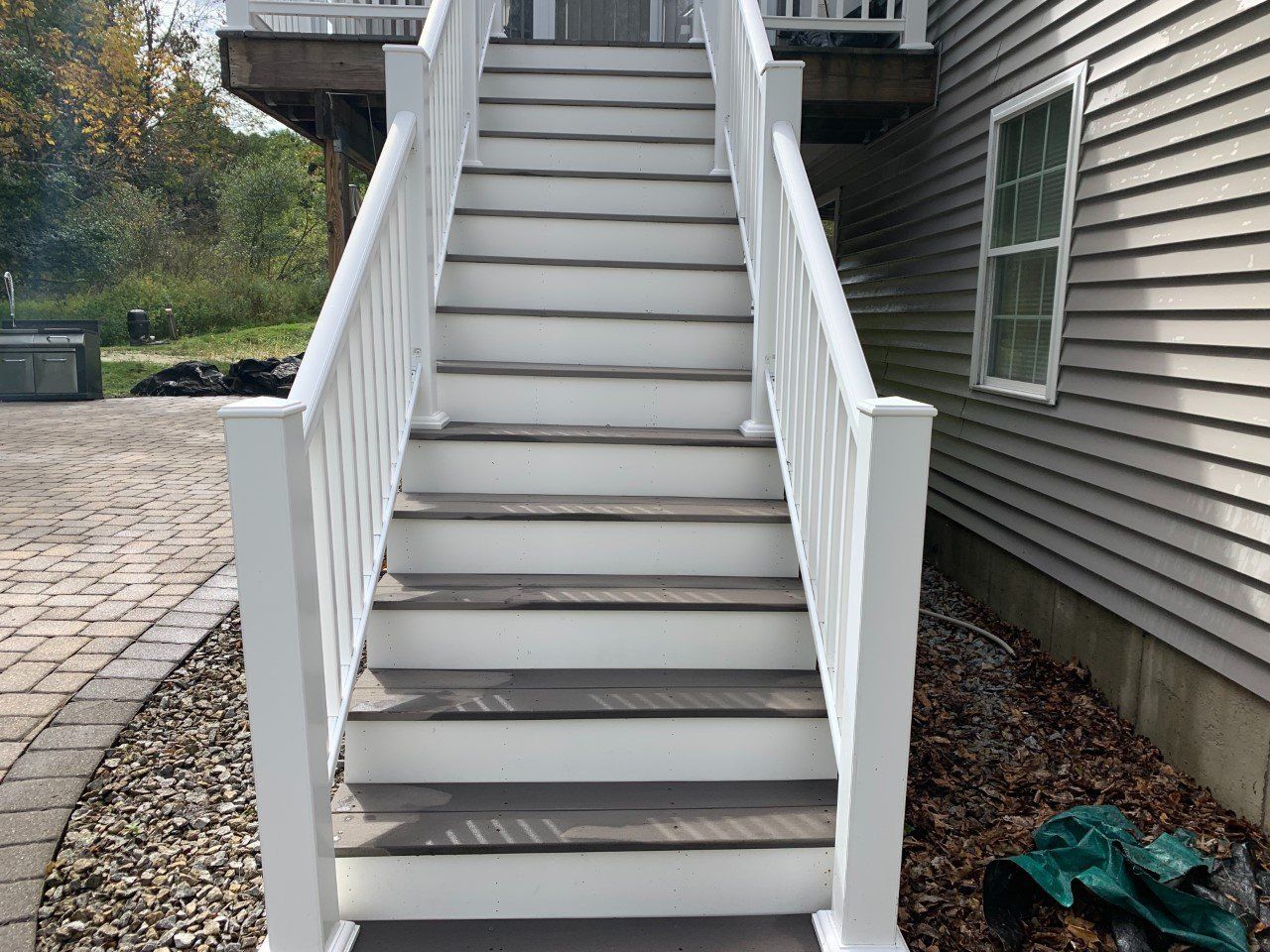 An outdoor set of stairs with white railings and gray steps leading up to a deck beside a gray-sided house.
