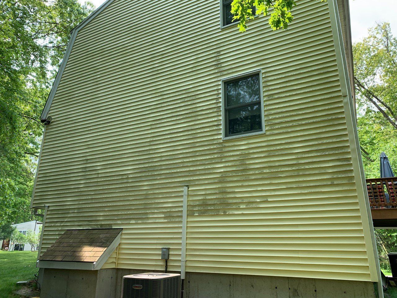 Yellow, two-story house with a brick chimney, three visible windows, and a red patio umbrella outdoors.