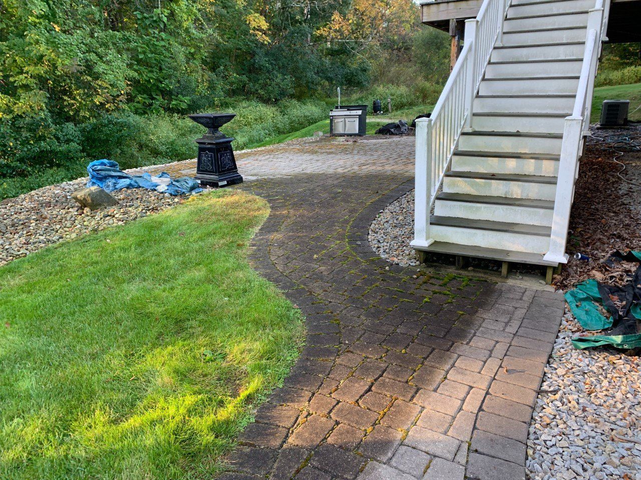 A brick walkway curves toward white stairs next to a green lawn and a gravel area with a decorative planter.