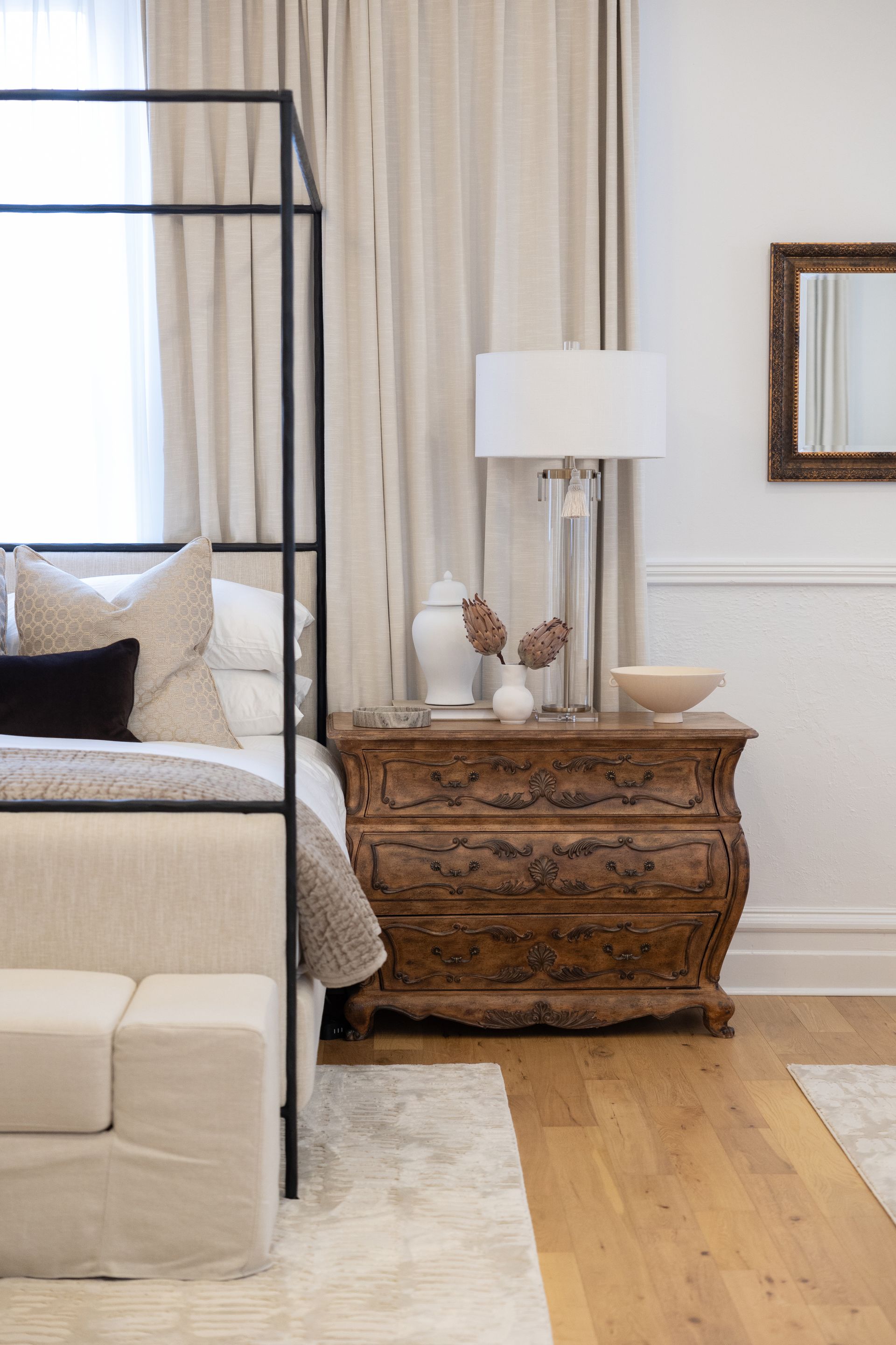 A bedroom with a canopy bed , nightstand , lamp and mirror.