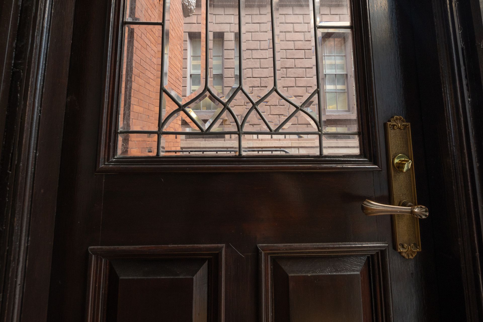 A close up of a door with a stained glass window and a brick building in the background.