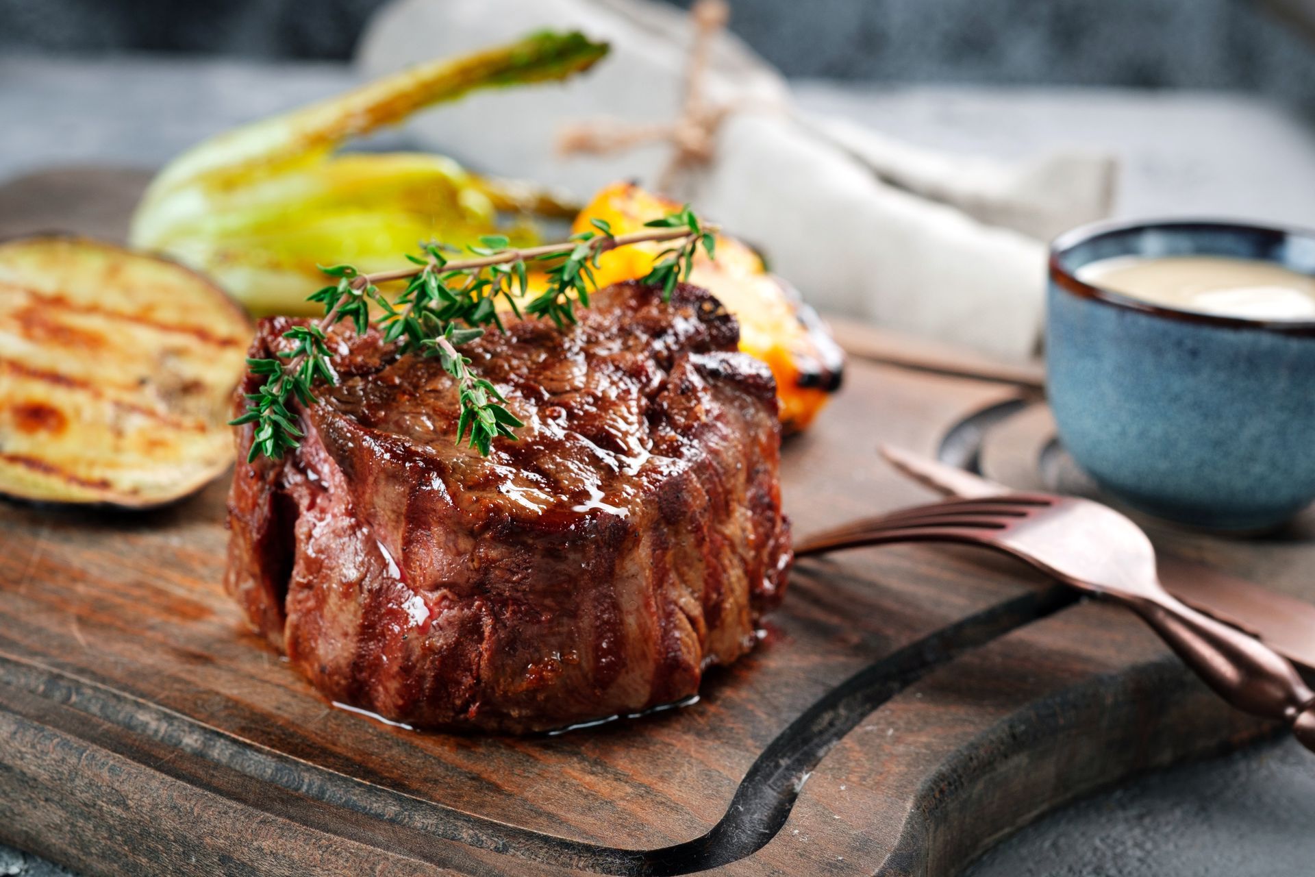 A steak is sitting on a wooden cutting board with vegetables.