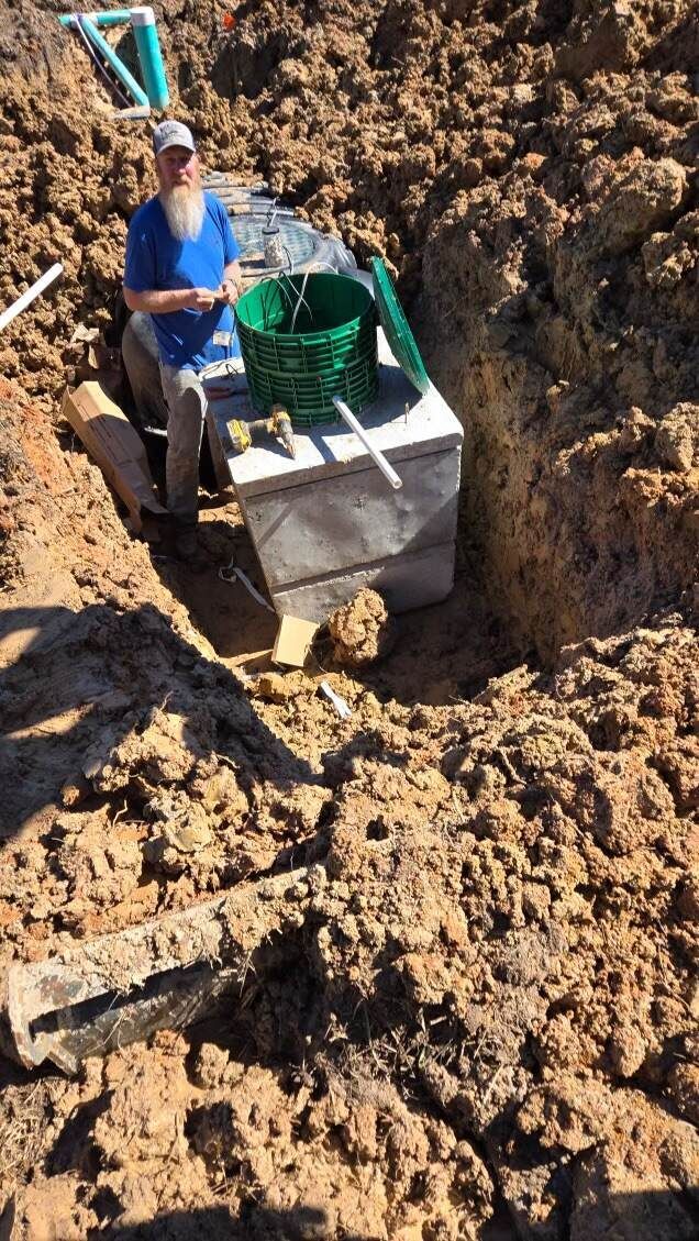 Man near a concrete septic tank in an open trench, dirt surrounding.