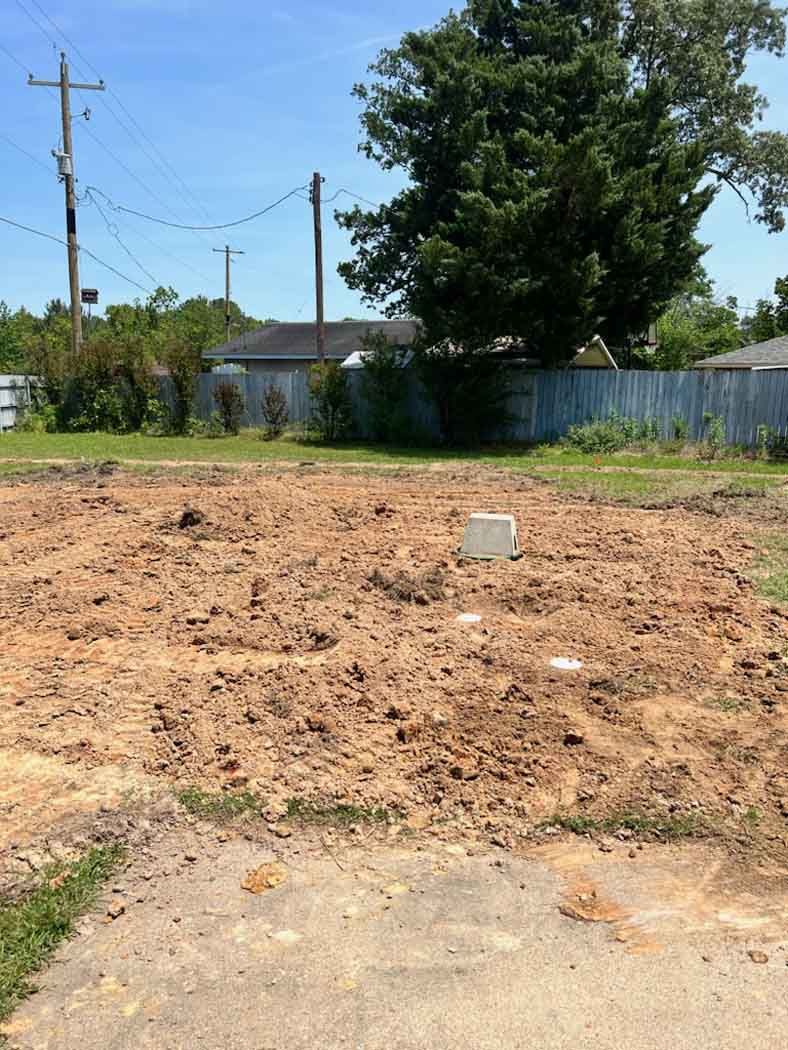 A cleared dirt lot, possibly for construction, under a bright blue sky.