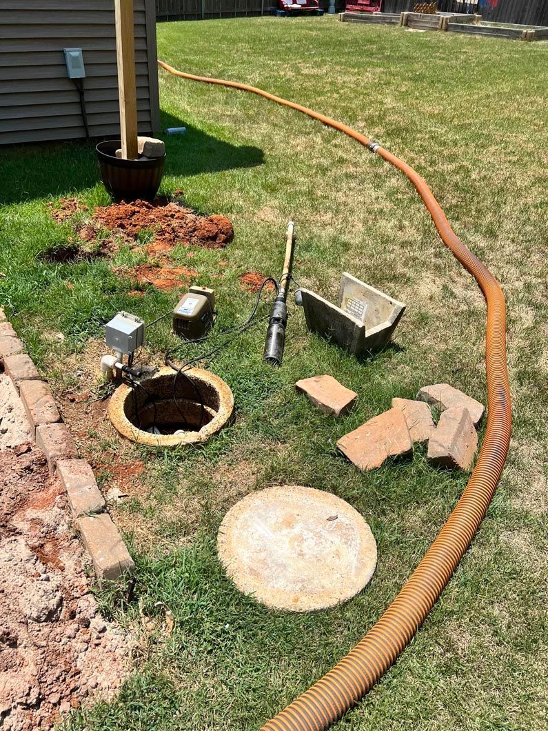 Outdoor scene with septic tank access point, hose, and tools.