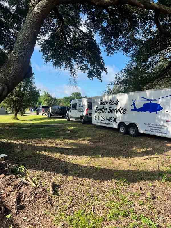 Septic service truck and trailer parked on grass under a tree.