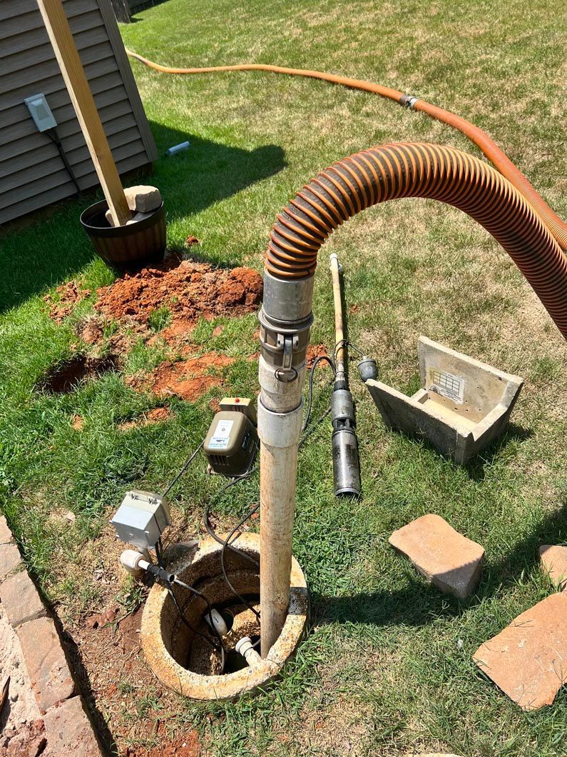 Well pump installation. Pipe and hose in a hole in the ground, equipment and dirt on grass.