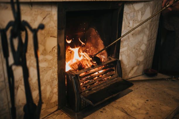 Cast iron fireplace with burning logs, open hearth fire and metal poker in cozy stone interior.