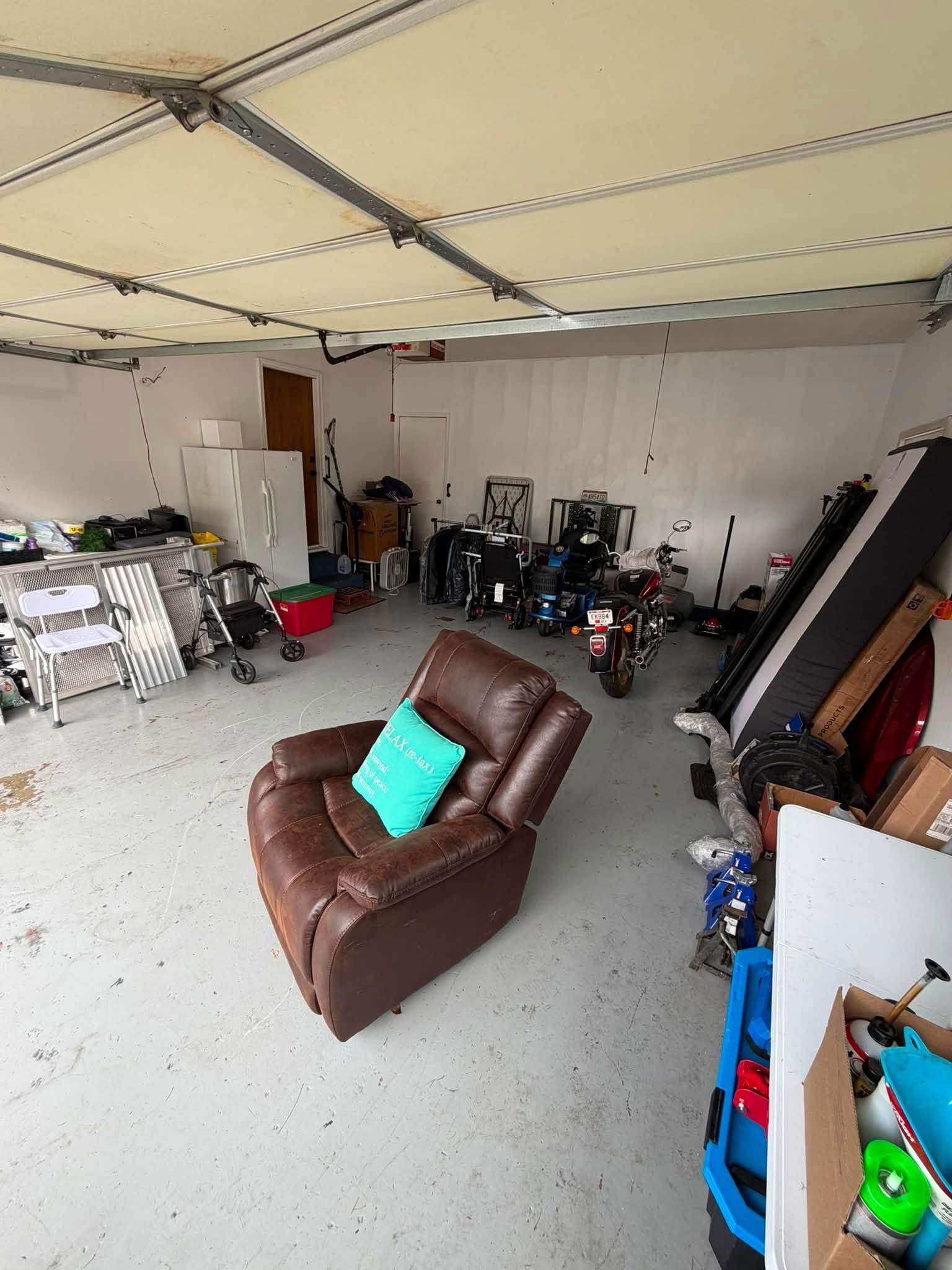 Garage with brown recliner chair, teal pillow, and assorted tools and equipment stored along the walls.