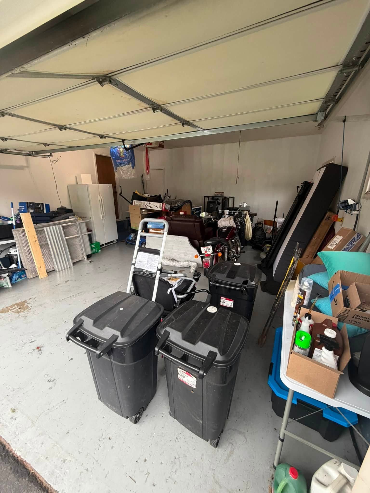 Cluttered garage with storage bins, tools, and boxes under an open door