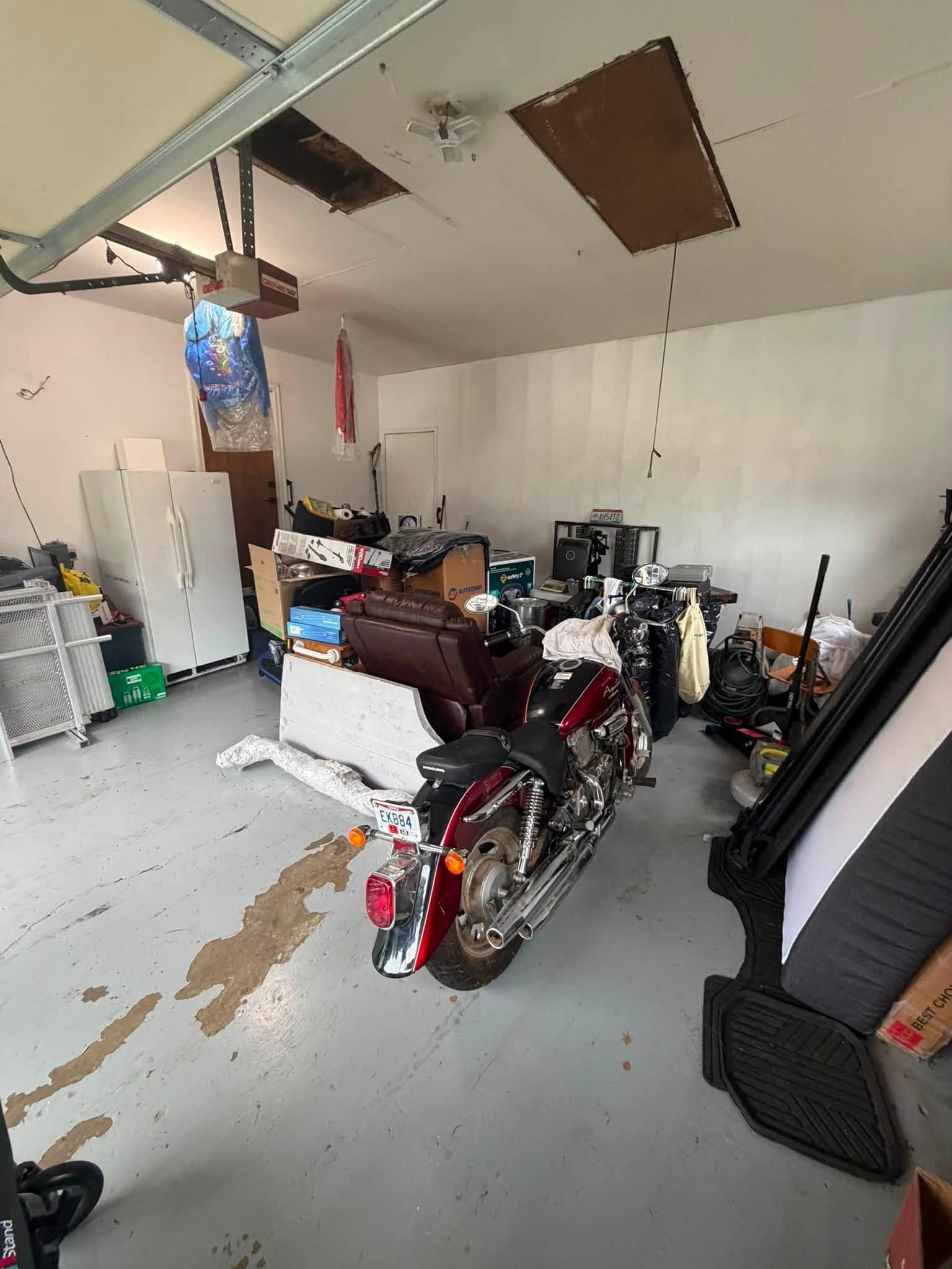 Cluttered garage with a motorcycle in the foreground, tools and storage items stacked around it.