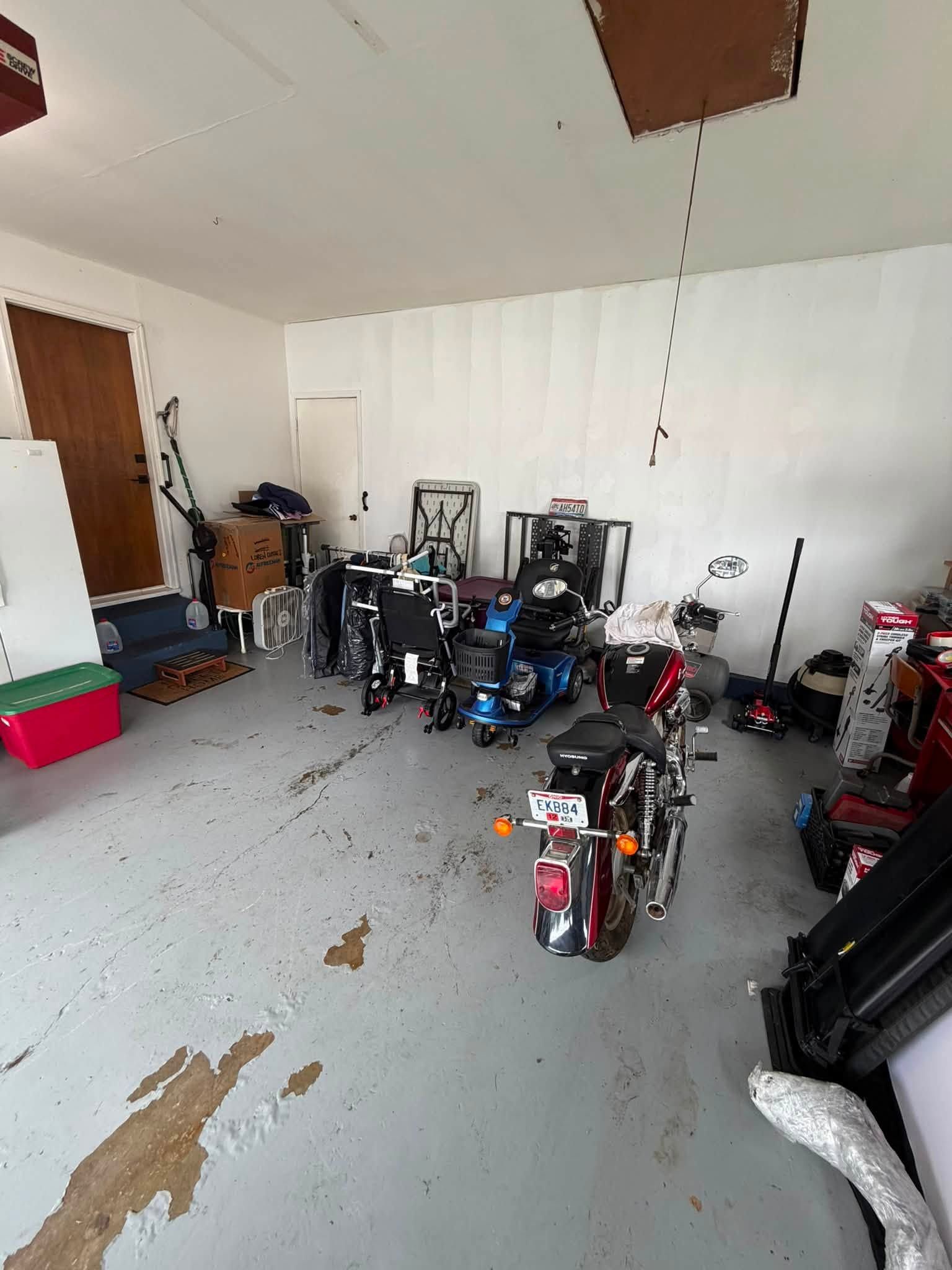 Cluttered garage with several motorcycles and tools on a gray floor, white walls, and an open wooden door