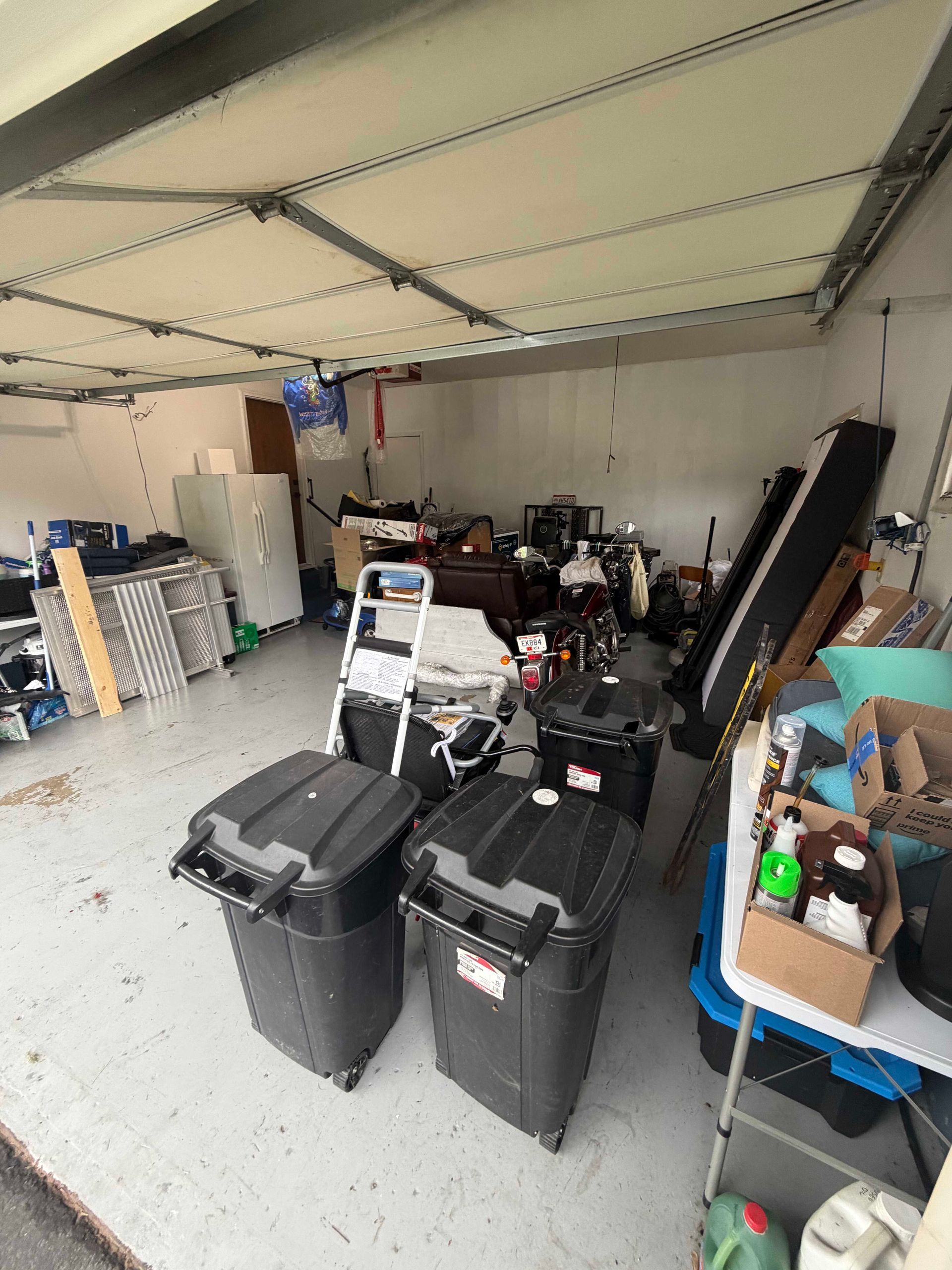 Cluttered garage with storage bins, tools, and stacked items under a closed door