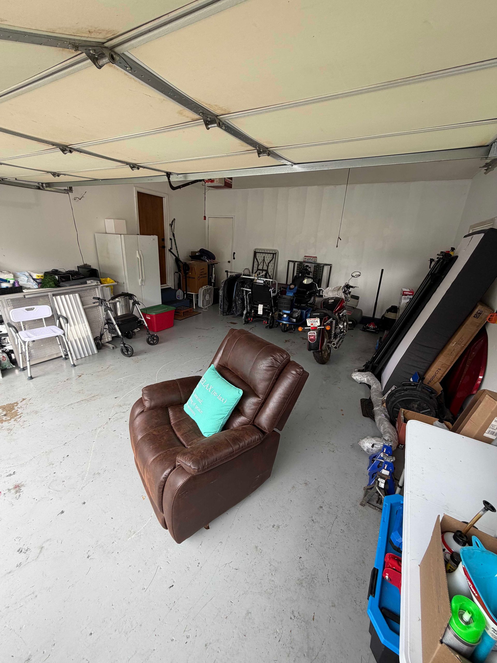 Garage with a brown recliner chair, stacked boxes, tools, and storage items scattered around.