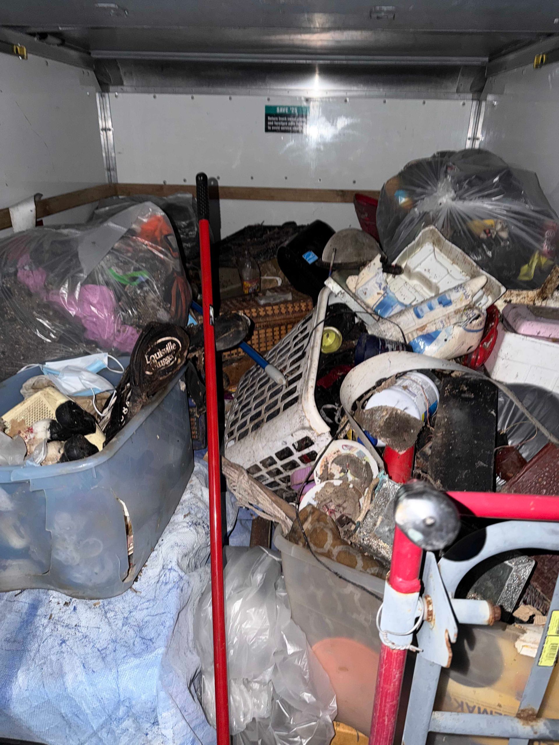 Cluttered storage area with piled boxes, bags, and household items packed tightly inside a small room.