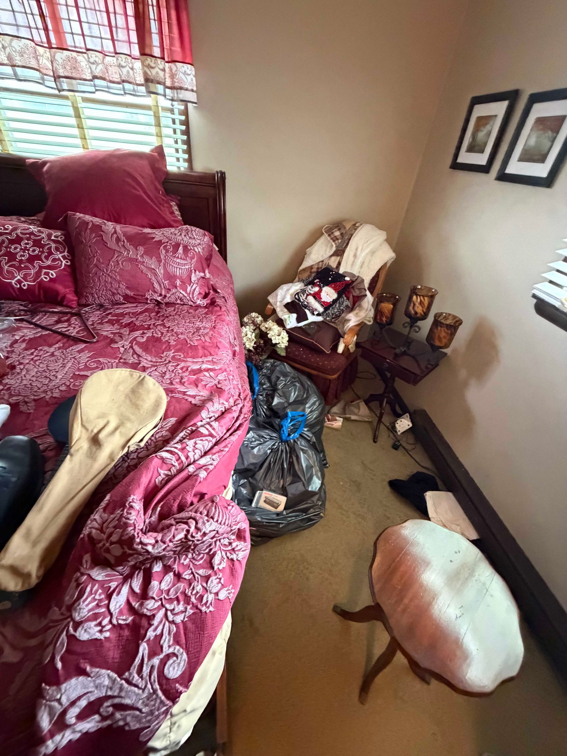 Cluttered living room with a red patterned chair, small side table, wall art, and a pet bed on the floor