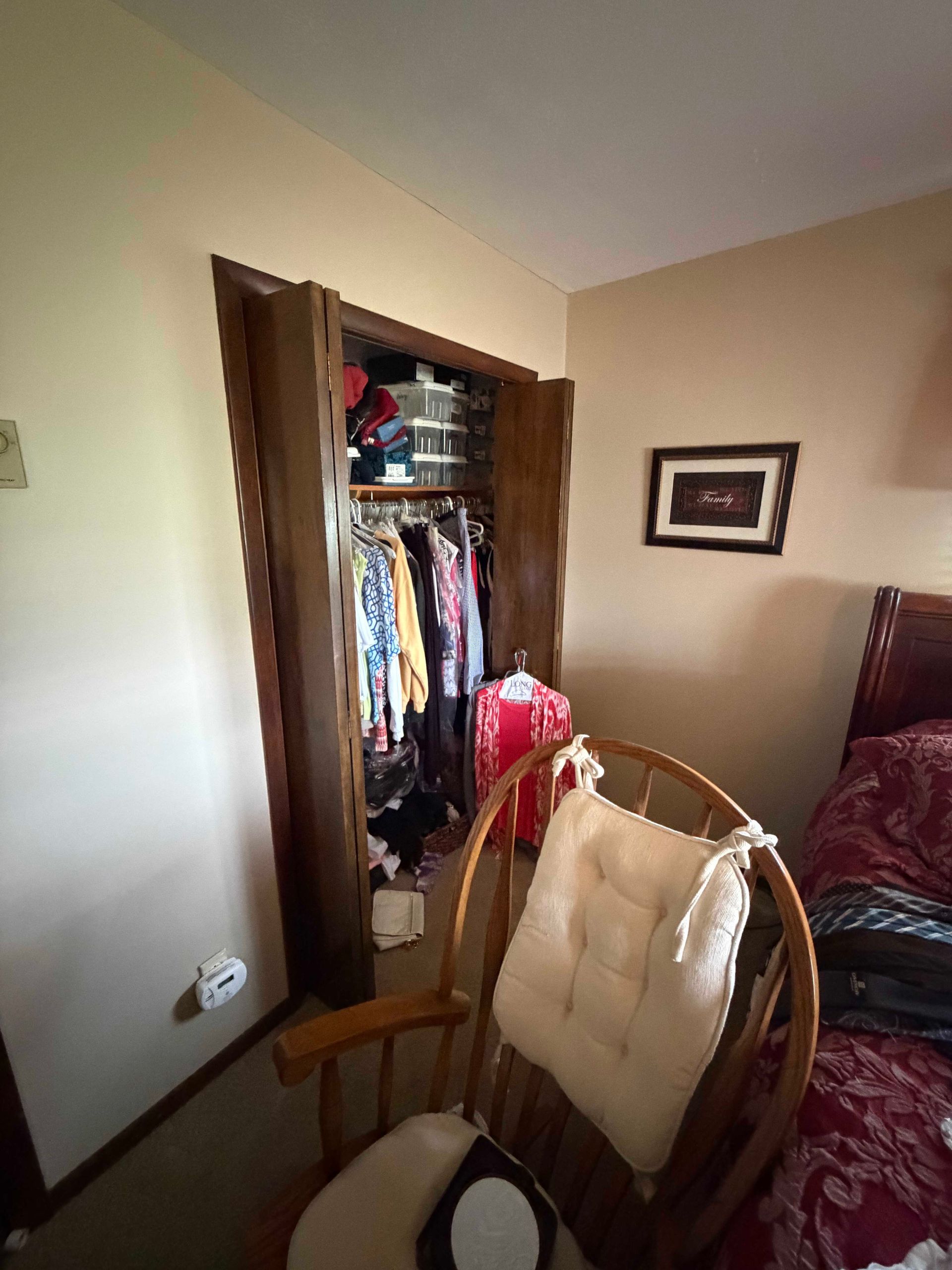 Bedroom with open closet, wooden chair, and bed with red bedspread.