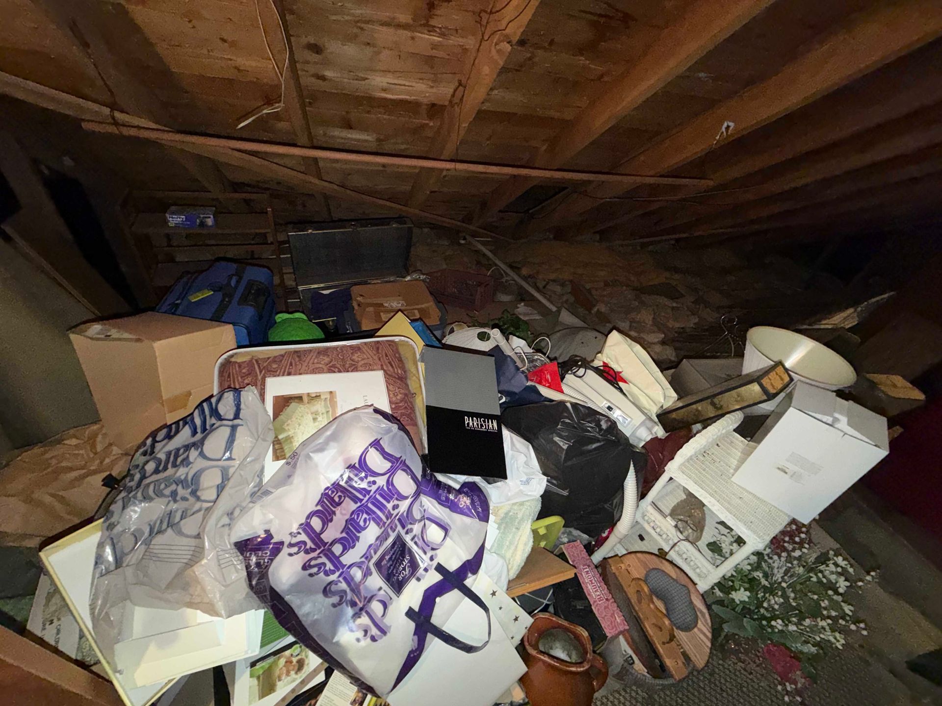 Cluttered attic with bags, boxes, and household items strewn across the floor.