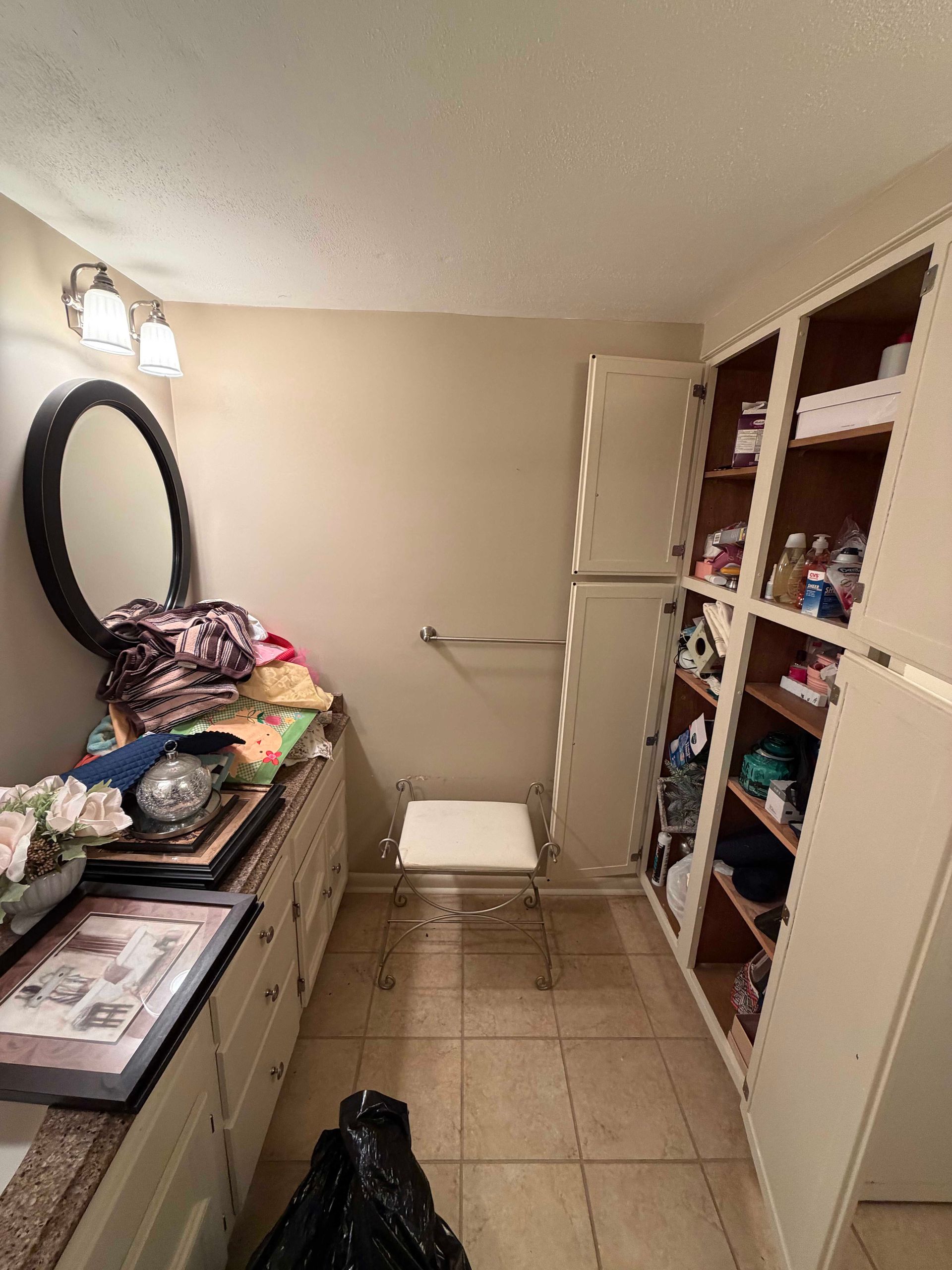 Small dressing room with open closet, dresser, mirror, and stool on tiled floor.
