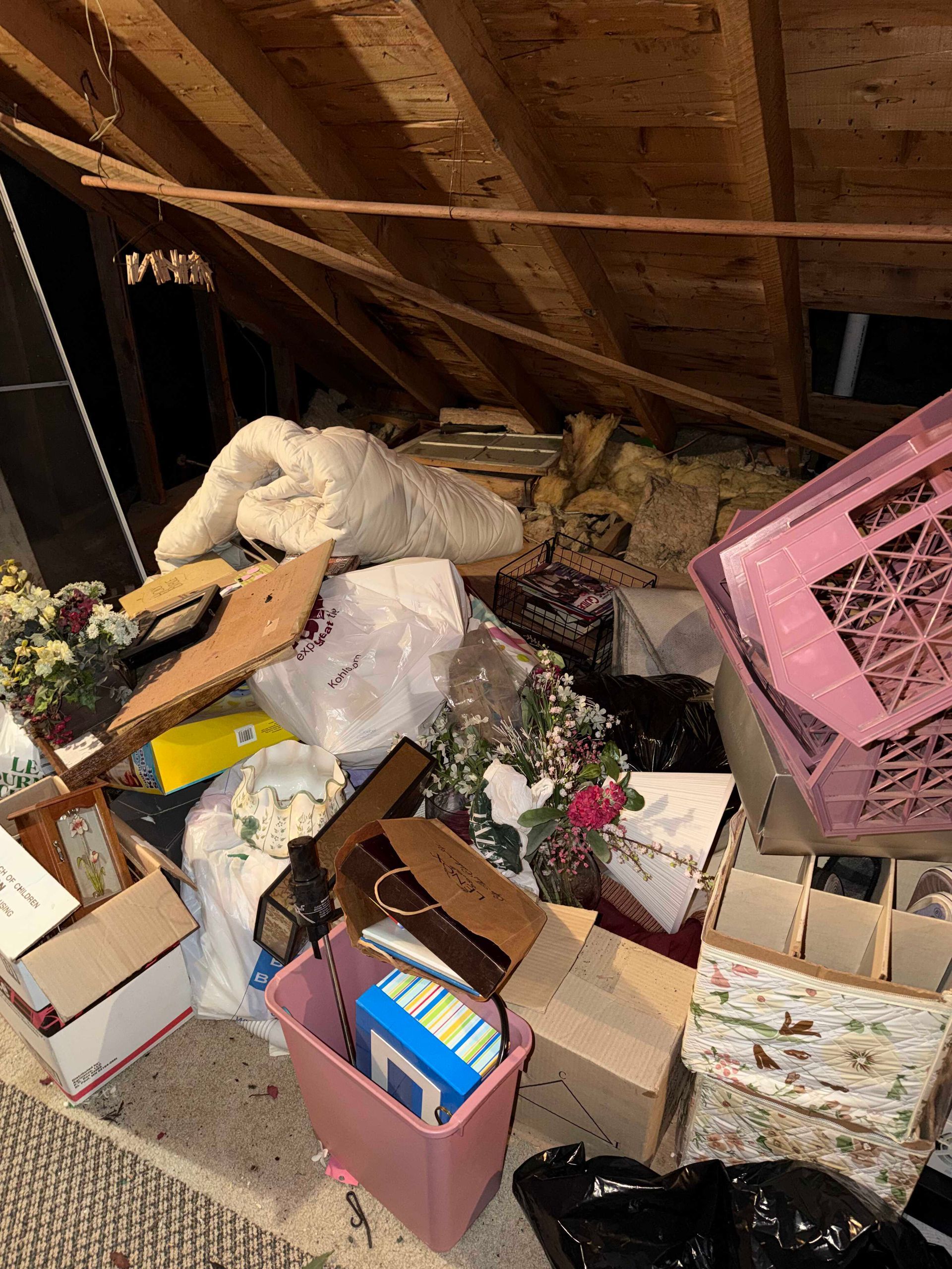 Cluttered attic with piled boxes, bags, and debris under exposed wooden beams