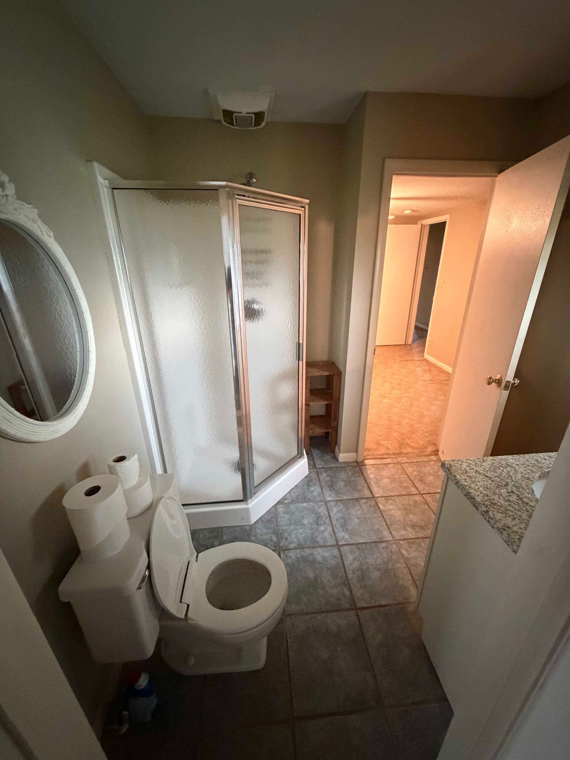 Small bathroom with tiled floor, shower stall, toilet, sink, and an open door to a hallway.