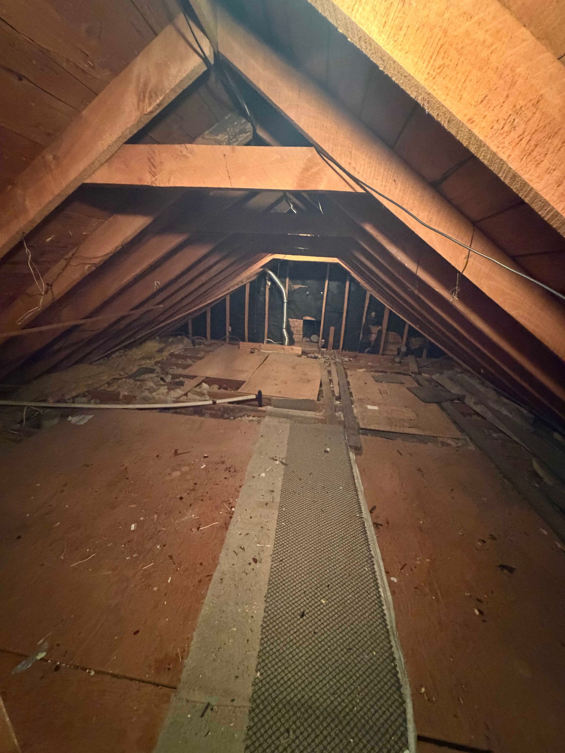Attic interior with exposed wooden beams, insulation, and a narrow walkway down the center