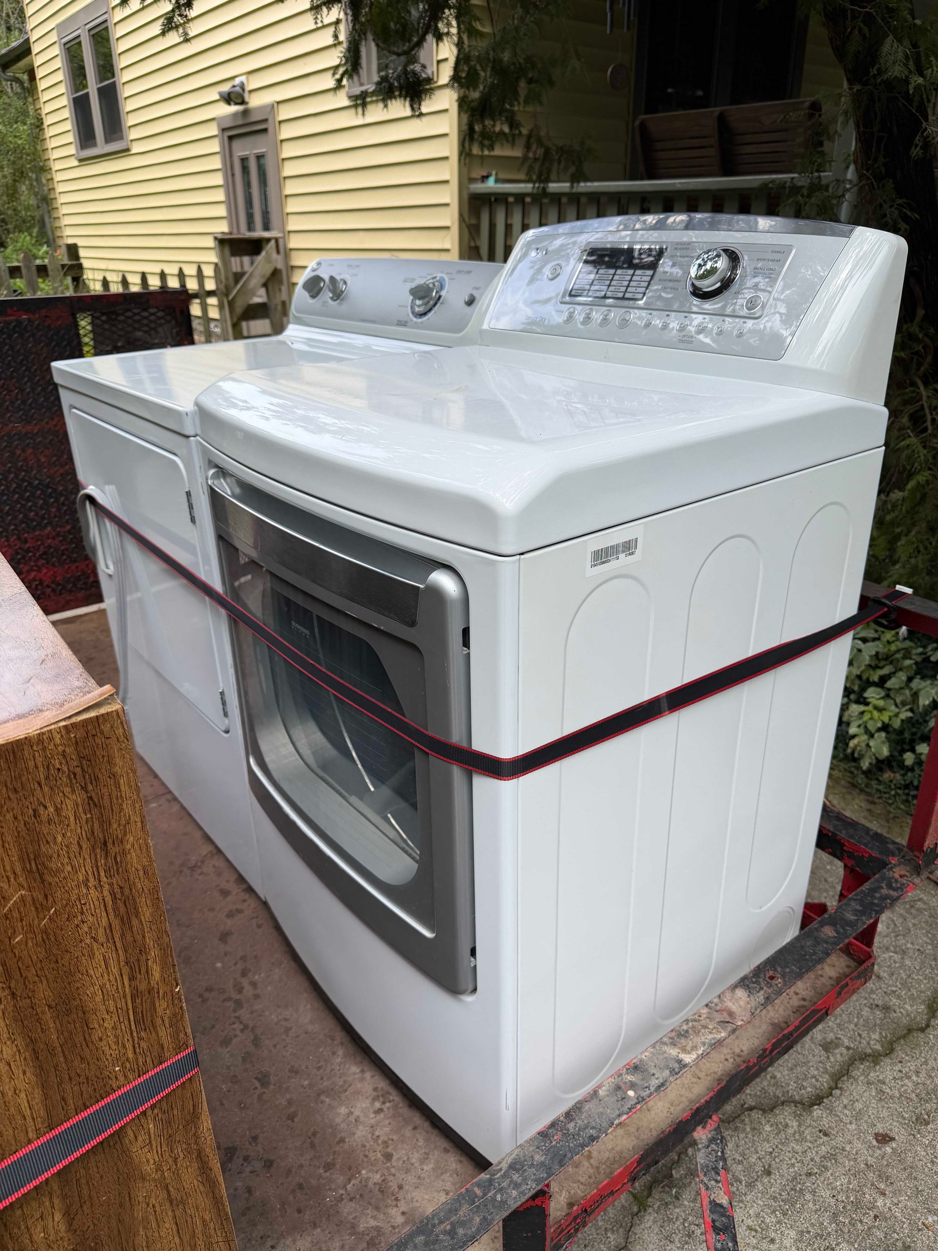 White washer and dryer strapped together on a dolly outside a house.