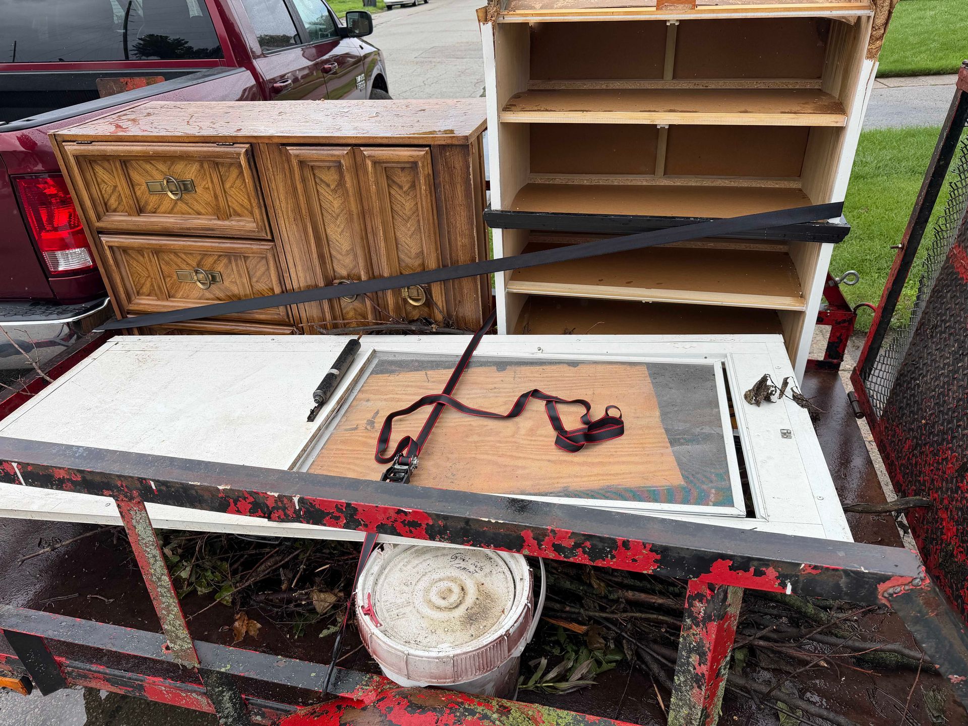 Disassembled furniture and cabinets strapped on a trailer, with a white tabletop and red metal frame.