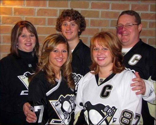 A group of five people wearing Pittsburgh Penguins hockey jerseys pose in front of a brick wall.