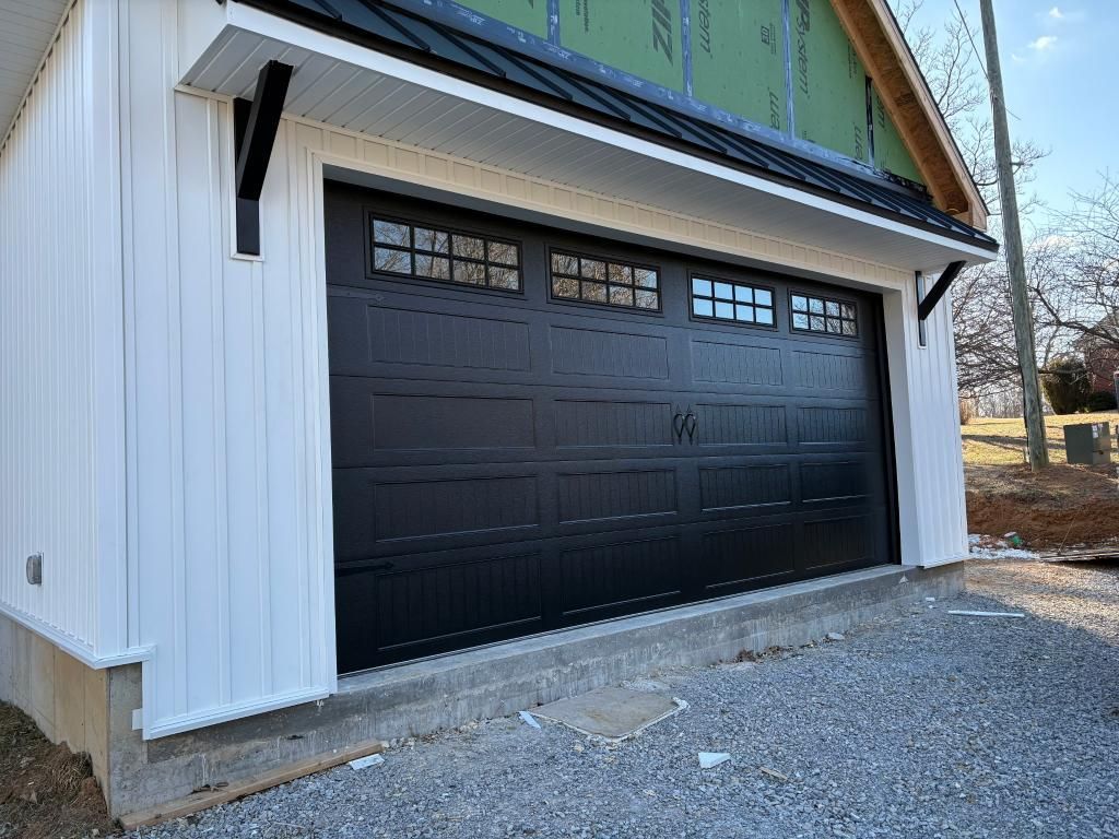 Black garage door with windows, white siding, and gravel driveway.