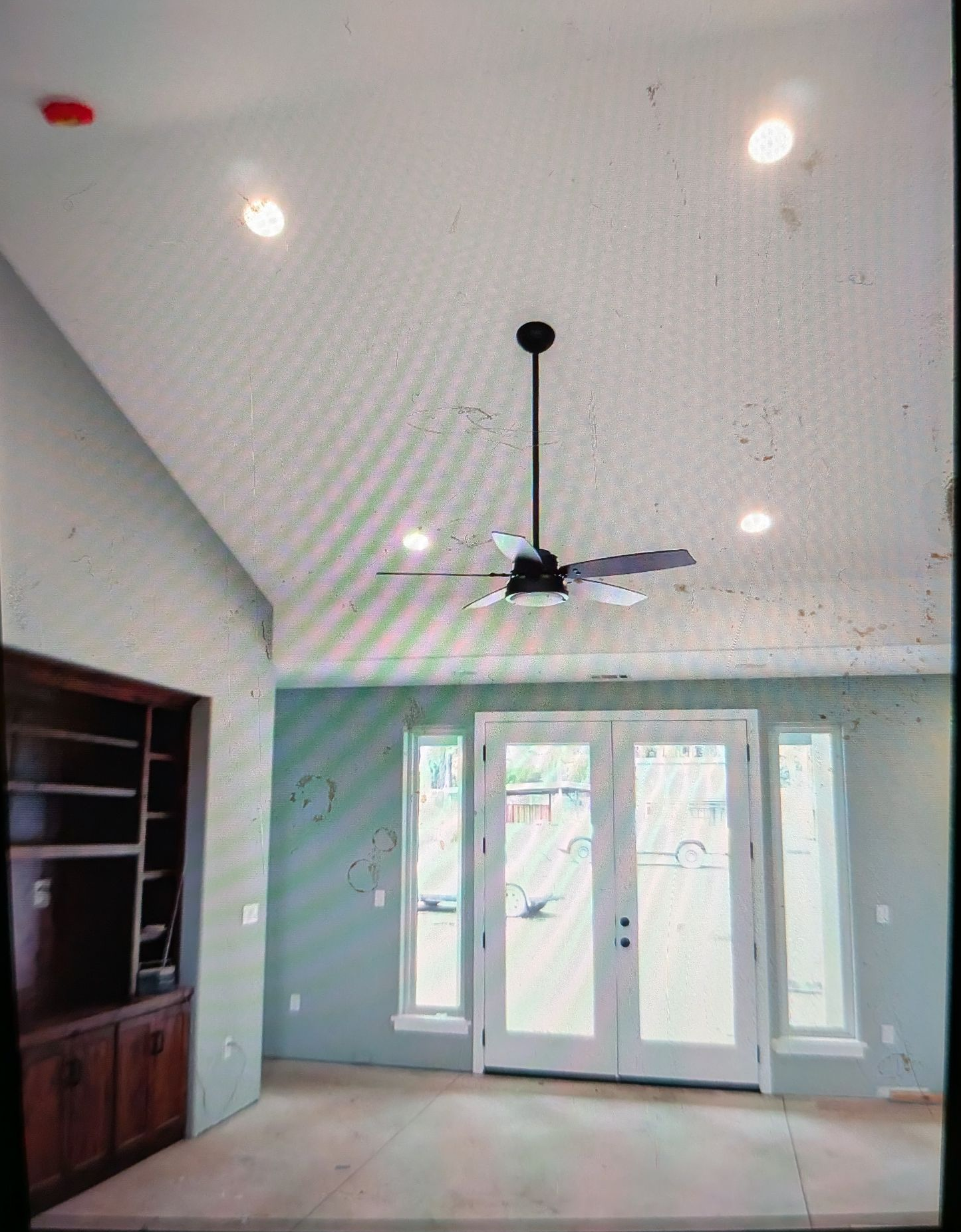 A light blue room with a vaulted ceiling, a ceiling fan, French doors, and a built-in bookshelf.