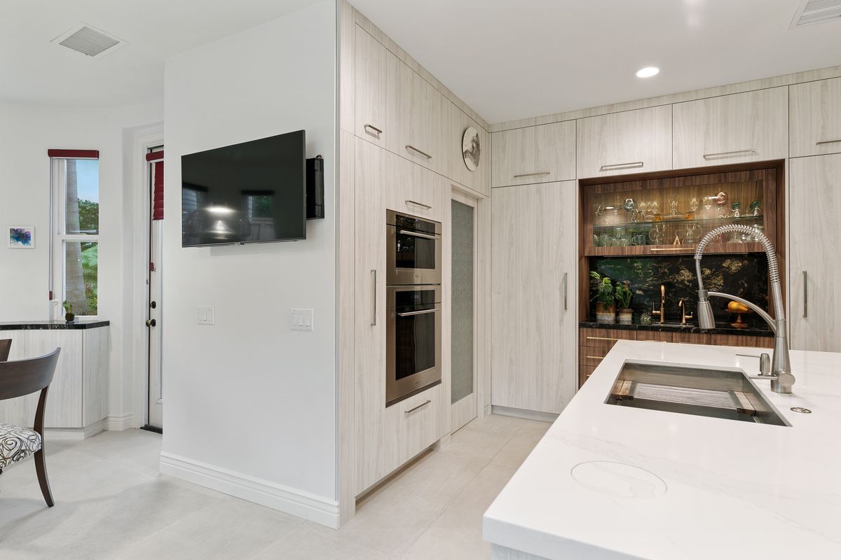 A kitchen with white cabinets and a flat screen tv on the wall.
