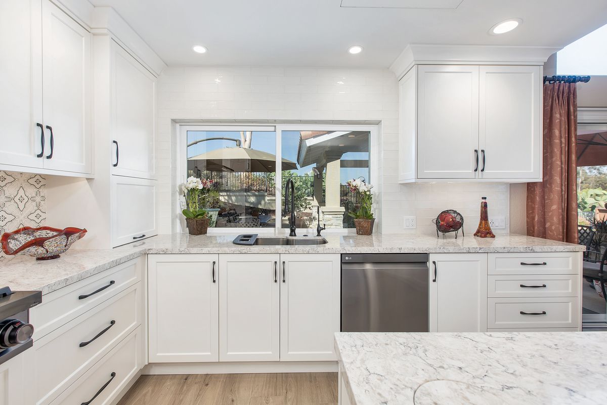 A kitchen with white cabinets , granite counter tops , stainless steel appliances and a large window.